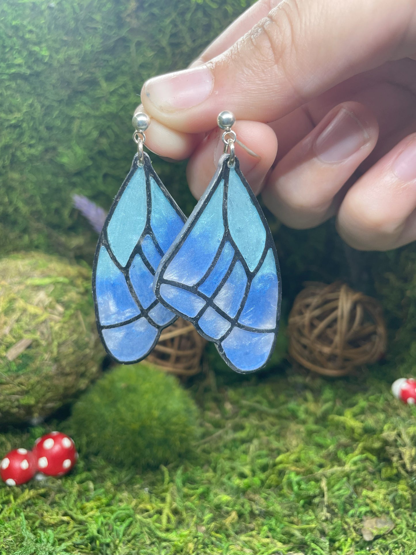 Blue butterfly wing earrings held by a hand against a natural background