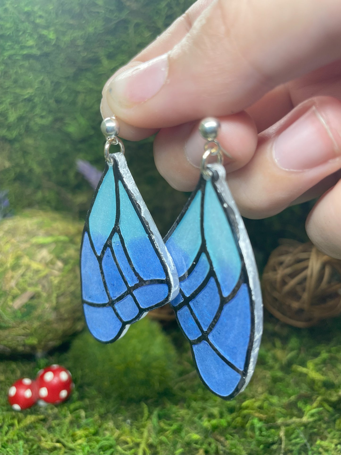 Blue butterfly-shaped earrings held by a hand against a natural background